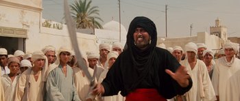 Movie still from “Raiders of the Lost Ark” (1981), directed by Steven Spielberg – A man holding a sword in front of a group of people; Medium shot, Low angle