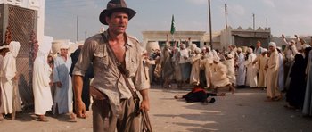 Movie still from “Raiders of the Lost Ark” (1981), directed by Steven Spielberg – A man in an indiana jones outfit standing in front of a crowd of people; Medium shot, Over the shoulder angle