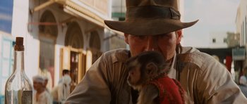 Movie still from “Raiders of the Lost Ark” (1981), directed by Steven Spielberg – A man holding a baby monkey in his arms; Close Up shot, Over the shoulder angle