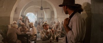 Movie still from “Raiders of the Lost Ark” (1981), directed by Steven Spielberg – A group of men sitting at a table in front of a building; Wide shot, Over the shoulder angle