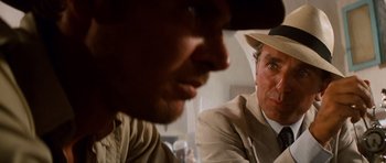 Movie still from “Raiders of the Lost Ark” (1981), directed by Steven Spielberg – A man in a suit and a man in a hat looking at each other; Close Up shot, Over the shoulder angle