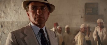 Movie still from “Raiders of the Lost Ark” (1981), directed by Steven Spielberg – A man in a suit and a hat standing in front of a group of men; Close Up shot, Over the shoulder angle