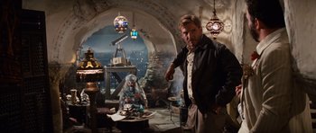 Movie still from “Raiders of the Lost Ark” (1981), directed by Steven Spielberg – A man standing next to a woman sitting on a chair; Wide shot, Over the shoulder angle