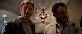 Movie still from “Raiders of the Lost Ark” (1981), directed by Steven Spielberg – A couple of men standing next to each other in a room; Close Up shot, Over the shoulder angle