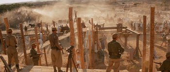 Movie still from “Raiders of the Lost Ark” (1981), directed by Steven Spielberg – A group of men standing next to each other on a dirt field; Wide shot, Over the shoulder angle