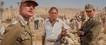 Movie still from “Raiders of the Lost Ark” (1981), directed by Steven Spielberg – An old man in a white shirt is standing in front of a group of people; Medium shot, Over the shoulder angle