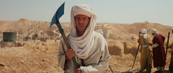 Movie still from “Raiders of the Lost Ark” (1981), directed by Steven Spielberg – A man holding a shovel while standing in the desert; Close Up shot, Over the shoulder angle
