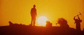 Movie still from “Raiders of the Lost Ark” (1981), directed by Steven Spielberg – A man standing on top of a hill in front of the sun; Wide shot, Low angle