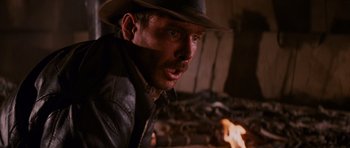 Movie still from “Raiders of the Lost Ark” (1981), directed by Steven Spielberg – A person wearing a hat near a fire; Close Up shot, Over the shoulder angle