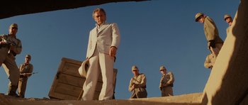 Movie still from “Raiders of the Lost Ark” (1981), directed by Steven Spielberg – A man in a white suit standing in front of two other men; Wide shot, Low angle