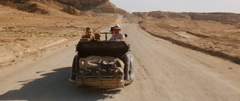 Movie still from “Raiders of the Lost Ark” (1981), directed by Steven Spielberg – Two men driving a car down a dirt road; Wide shot, High angle