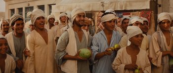 Movie still from “Raiders of the Lost Ark” (1981), directed by Steven Spielberg – A group of men standing next to each other holding fruit; Medium shot, Over the shoulder angle