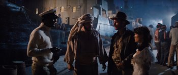 Movie still from “Raiders of the Lost Ark” (1981), directed by Steven Spielberg – A man in a turban and a man in a hat and a man in a suit and tie; Medium shot, Over the shoulder angle
