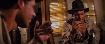 Movie still from “Raiders of the Lost Ark” (1981), directed by Steven Spielberg – A man in a hat and a man in a trench coat talking to another man; Close Up shot, Over the shoulder angle