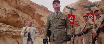 Movie still from “Raiders of the Lost Ark” (1981), directed by Steven Spielberg – A man in a military uniform standing in front of a flag; Medium shot, Low angle