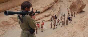 Movie still from “Raiders of the Lost Ark” (1981), directed by Steven Spielberg – A group of men in military garb walking down a dirt road; Wide shot, Over the shoulder angle