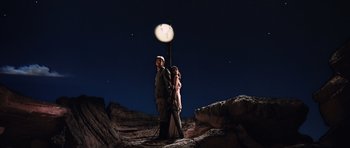 Movie still from “Raiders of the Lost Ark” (1981), directed by Steven Spielberg – A man and a woman standing next to a street light at night; Wide shot, Low angle