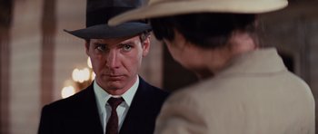 Movie still from “Raiders of the Lost Ark” (1981), directed by Steven Spielberg – A man wearing a suit and a hat looking at a woman; Close Up shot, Over the shoulder angle
