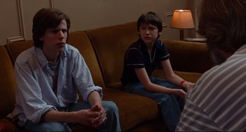 Movie still from “The Squid and the Whale” (2005), directed by Noah Baumbach – Two people sitting on a brown couch in front of a lamp; Medium shot, Over the shoulder angle