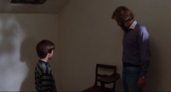 Movie still from “The Squid and the Whale” (2005), directed by Noah Baumbach – A man and a boy standing next to each other in front of a wooden chair; Medium shot, Over the shoulder angle