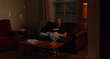 Movie still from “The Squid and the Whale” (2005), directed by Noah Baumbach – A man sitting on top of a brown couch in a living room; Wide shot, High angle