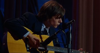 Movie still from “The Squid and the Whale” (2005), directed by Noah Baumbach – A man in a suit playing an acoustic guitar on a stage; Close Up shot, High angle