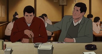 Movie still from “The Summit of the Gods” (2021), directed by Patrick Imbert – Two men sitting at a table in front of plates of food; Medium shot, Over the shoulder angle