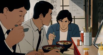 Movie still from “The Summit of the Gods” (2021), directed by Patrick Imbert – Two men are sitting at a table with a bowl of food; Medium shot, Over the shoulder angle