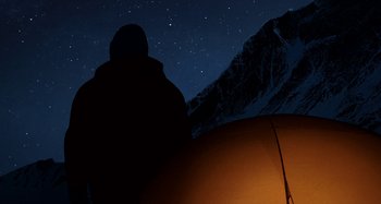 Movie still from “The Summit of the Gods” (2021), directed by Patrick Imbert – A person standing next to a tent in the night sky; Extreme Wide shot, Low angle