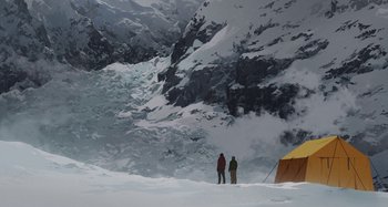 Movie still from “The Summit of the Gods” (2021), directed by Patrick Imbert – Two people standing in the snow next to a tent; Extreme Wide shot, Low angle