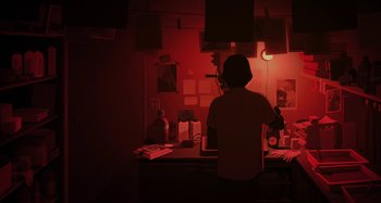 Movie still from “The Summit of the Gods” (2021), directed by Patrick Imbert – A person standing at a desk in a dark room; Wide shot, High angle