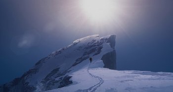 Movie still from “The Summit of the Gods” (2021), directed by Patrick Imbert – A person on a snow covered slope with a mountain in the background; Extreme Wide shot, Low angle