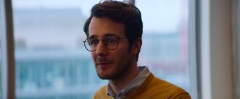 Movie still from “The Takedown” (2022), directed by Louis Leterrier – A person wearing glasses and a yellow sweater; Close Up shot, Over the shoulder angle