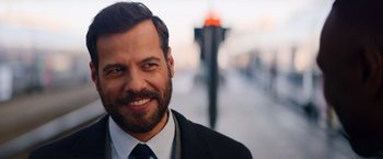 Movie still from “The Takedown” (2022), directed by Louis Leterrier – A person wearing a suit and tie; Close Up shot, Over the shoulder angle