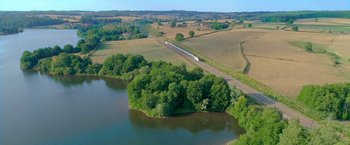 Movie still from “The Takedown” (2022), directed by Louis Leterrier – An aerial view of a train on the tracks near a body of water; Extreme Wide shot, High angle