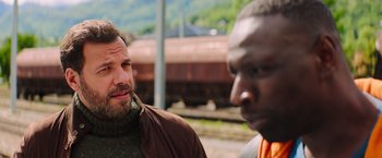 Movie still from “The Takedown” (2022), directed by Louis Leterrier – Two men are standing next to each other on the train tracks; Close Up shot, Over the shoulder angle
