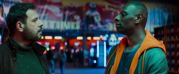 Movie still from “The Takedown” (2022), directed by Louis Leterrier – A man standing in front of a neon lit building; Close Up shot, Low angle