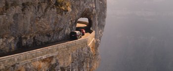 Movie still from “The Takedown” (2022), directed by Louis Leterrier – A couple of cars driving down a road on top of a cliff; Extreme Wide shot, High angle