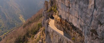 Movie still from “The Takedown” (2022), directed by Louis Leterrier – A road going through a cave on the side of a mountain; Extreme Wide shot, High angle