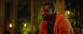 Movie still from “The Takedown” (2022), directed by Louis Leterrier – A man in an orange jacket is sitting outside; Close Up shot, Over the shoulder angle