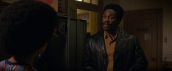 Movie still from “The Trial of the Chicago 7” (2020), directed by Aaron Sorkin – A man wearing a leather jacket standing next to a refrigerator; Medium shot, Over the shoulder angle