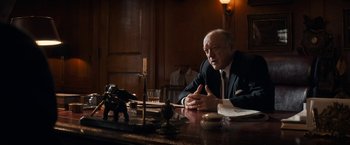 Movie still from “The Trial of the Chicago 7” (2020), directed by Aaron Sorkin – An older man sitting at a table in front of an elephant statue; Medium shot, Over the shoulder angle
