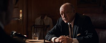 Movie still from “The Trial of the Chicago 7” (2020), directed by Aaron Sorkin – An older man sitting at a table with a glass of whiskey; Medium shot, Over the shoulder angle