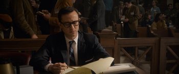 Movie still from “The Trial of the Chicago 7” (2020), directed by Aaron Sorkin – A man sitting at a table looking at a book; Medium shot, High angle