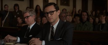 Movie still from “The Trial of the Chicago 7” (2020), directed by Aaron Sorkin – A man in a suit and tie sitting in front of a group of people; Medium shot, Over the shoulder angle