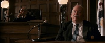 Movie still from “The Trial of the Chicago 7” (2020), directed by Aaron Sorkin – A man sitting in front of a microphone in a courtroom; Medium shot, Over the shoulder angle