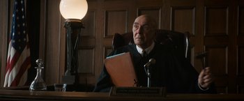 Movie still from “The Trial of the Chicago 7” (2020), directed by Aaron Sorkin – An older man sitting at a desk in a courtroom; Medium shot, Low angle