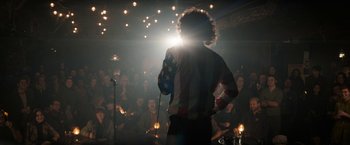 Movie still from “The Trial of the Chicago 7” (2020), directed by Aaron Sorkin – A man standing in front of a microphone in front of a group of onlookers; Wide shot, Over the shoulder angle