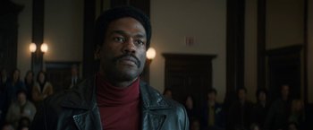 Movie still from “The Trial of the Chicago 7” (2020), directed by Aaron Sorkin – A man wearing a black leather jacket and a red shirt; Close Up shot, Low angle