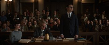 Movie still from “The Trial of the Chicago 7” (2020), directed by Aaron Sorkin – A man sitting at a table in front of a group of people; Medium shot, Over the shoulder angle